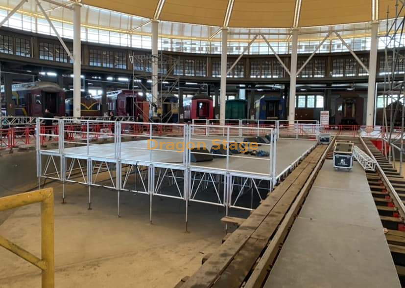  Podio de escenario con barandilla de aluminio de 12x8m con 2 escaleras de acceso y rampa de carga/descarga en el escenario trasero